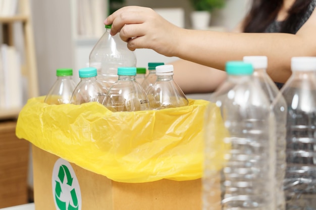 Home recycle eco groen nul concept Vrouw gooit lege plastic fles in de prullenbak met gele vuilniszakken thuis