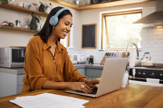 Foto lavoro a distanza a casa e donna d'affari sul laptop per la strategia del progetto di ricerca e la pianificazione in cucina freelancer sorriso e ragazza con le cuffie per la musica con documenti computer e lavoro online