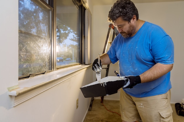 Home renovation in the handyman paints with a layer of white color paint brush a window molding frame