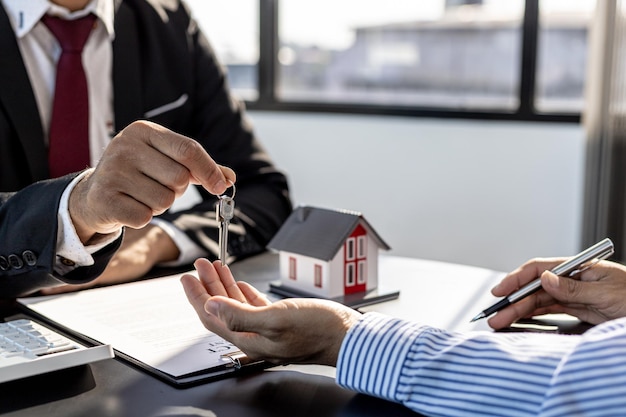 A home rental company employee is handing the house keys to a customer who has agreed to sign a rental contract, explaining the details and terms of the rental. Home and real estate rental ideas.