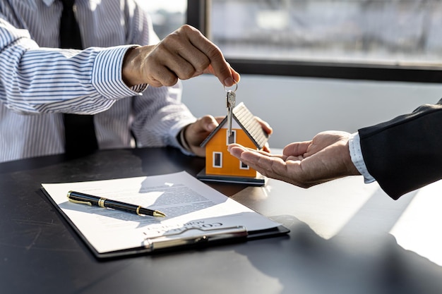 A home rental company employee is handing the house keys to a customer who has agreed to sign a rental contract, explaining the details and terms of the rental. Home and real estate rental ideas.