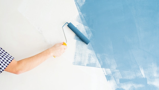 Home reparatie en verbetering. man kleurende muur blauw met een roller