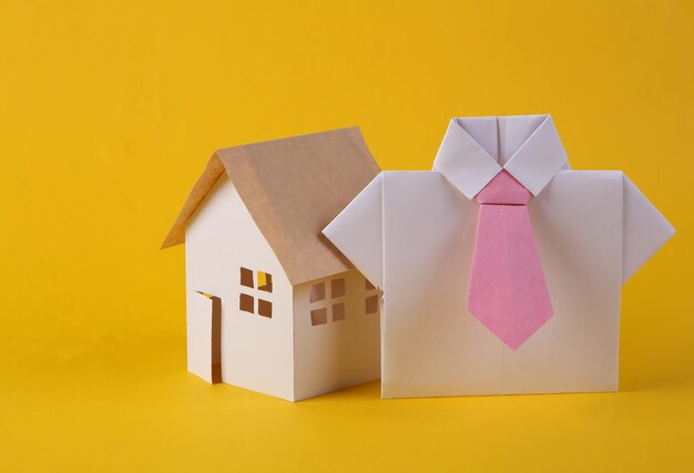 Home sale concept realtor origami shirt and house figurine on yellow background