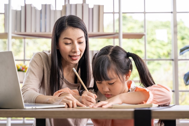Photo home schooling learning at home during virus pandemic. asian woman with her daughter in the living room , wearing surgical face masks to protect them from the virus.