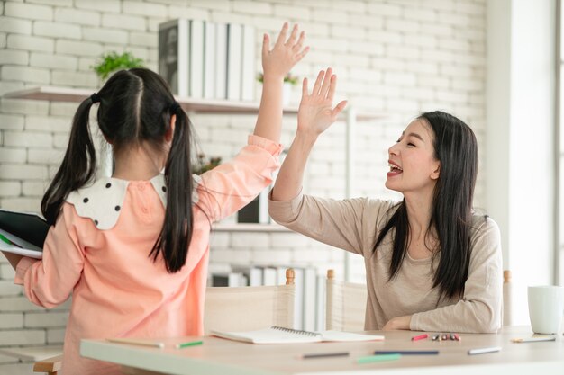 ウイルスパンデミック時の自宅でのホームスクーリング学習。リビングルームで娘と一緒にアジアの女性。ウイルスから保護するためにサージカルマスクを着用しています。