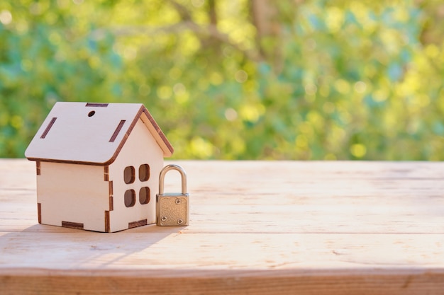 Home security concept: Wooden model house and lock on wooden surface.