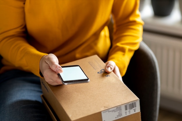 Foto shopping a domicilio e concetto di consegna a domicilio. mano femminile che tiene smartphone con schermo vuoto a casa