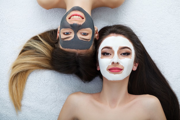 Home spa. Two women holding pieces of cucumber on their faces lying the bed.