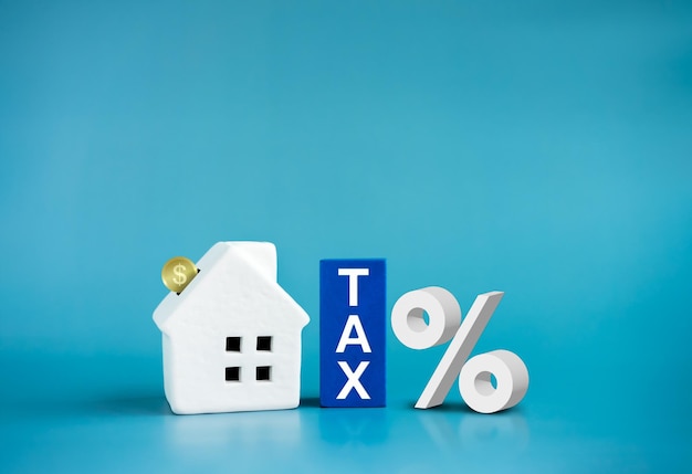 Home tax concept residential real estate property land building annual taxation Word Tax on blue blocks and coins fall in white small house percentage icon on blue background with copy space