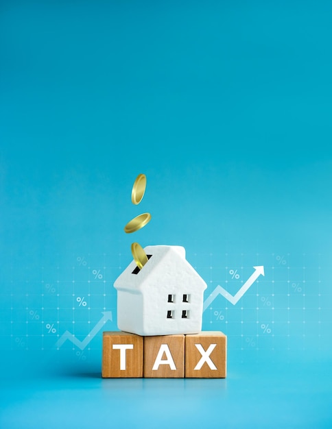 Home tax concept residential real estate property land building annual taxation Word Tax on wood blocks and coins fall in white small house percentage icon and rise up arrow on blue background