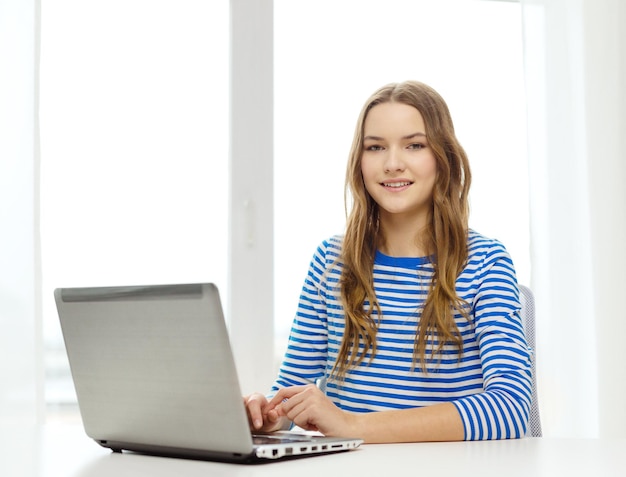 концепция дома, технологий и интернета - улыбающаяся девочка-подросток с ноутбуком дома