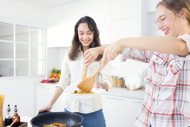 At home, two pals are having a good time in the kitchen. Sisters preparing spaghetti in the kitchen together. In the kitchen, two female pals