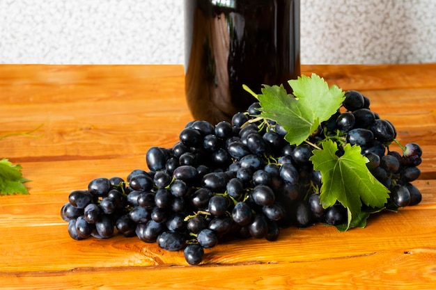 Foto vinificazione domestica un enorme pennello di uve fresche succose scure sullo sfondo di una bottiglia di vino