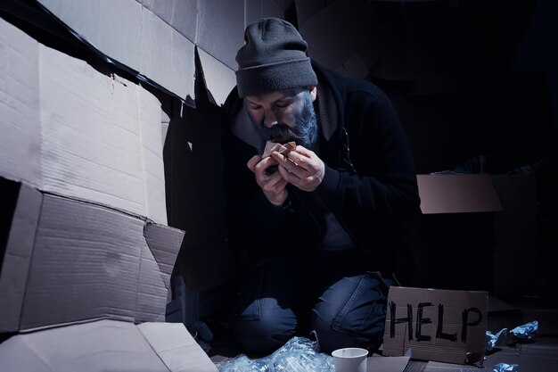 A homeless bearded man sits on boxes on the street and asks for help. Need a homeless person asks for money for food and overnight.