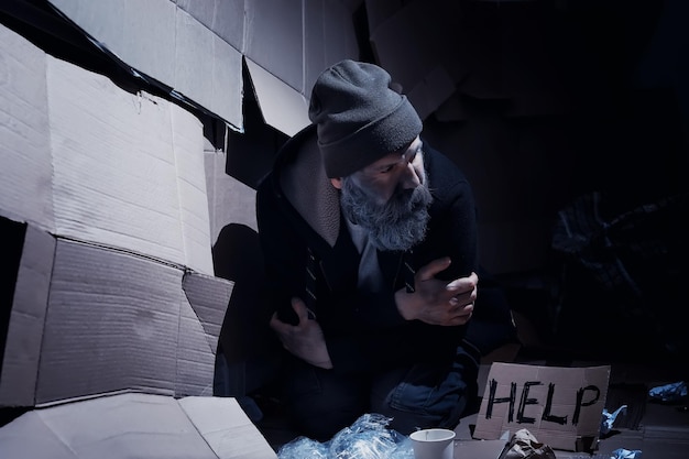 A homeless bearded man sits on boxes on the street and asks for help Need a homeless person asks for money for food and overnight