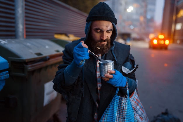 Homeless eating canned food on city street.