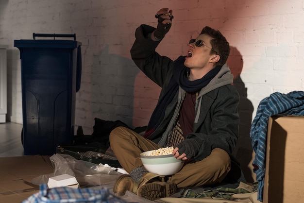 Homeless man eating popcorn while sitting on garbage dump