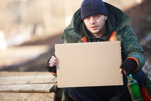 Homeless man holds blank cardboard for your text