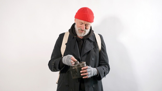 Photo homeless man, an old man with a gray beard in a hat smiling holding in his hand financial aid, dollars, isolated white background