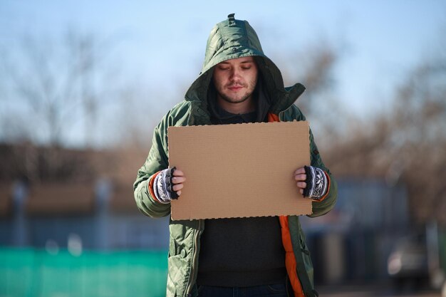 Homeless person with blanck cardboard. Focused on cardboard