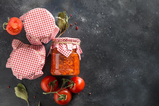 Homemade adjika in jar on black background Made of tomatoes garlic bell pepper and spice View from above Tunisia and Arabic cuisine adjika Regional food Paste harissa