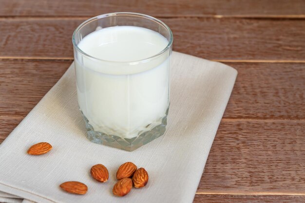 Homemade Almond milk in a glass and scattered nuts on wooden background copy space