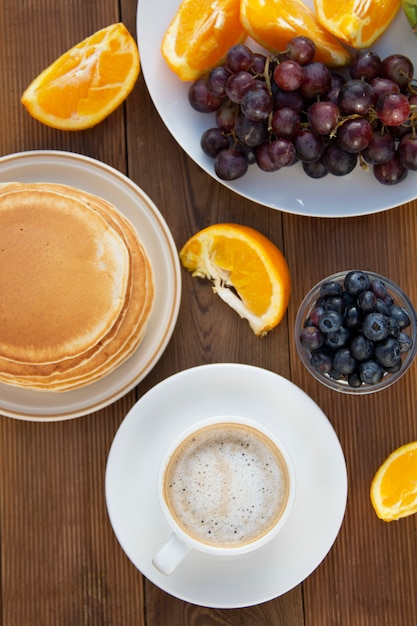 一杯のコーヒーとフルーツの自家製アメリカのパンケーキ。木製のテーブル