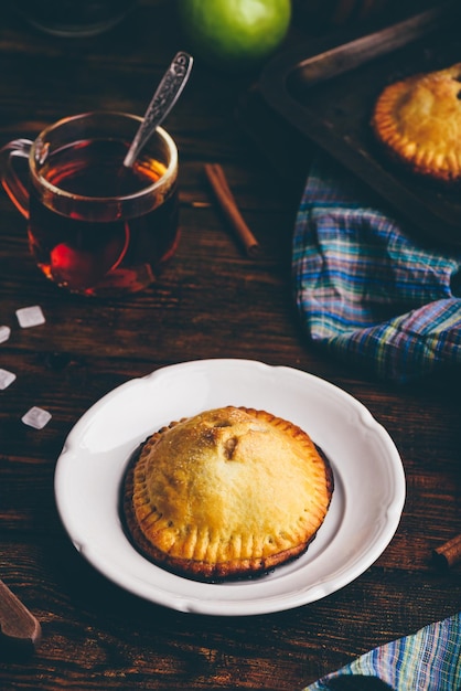 Homemade apple mini pie on white plate with cup of black tea