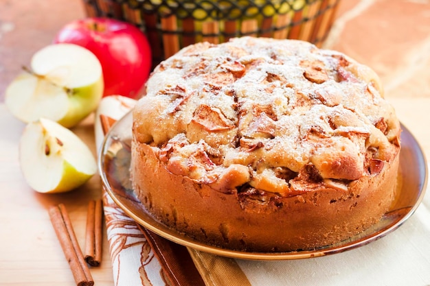 Torta di mele fatta in casa con cannella sul piatto e mele verdi e rosse sullo sfondo