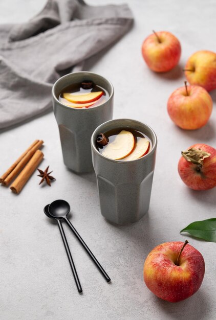 Homemade apple punch with apples and cinnamon in gray cups on a light background with fresh fruits and spices The concept of an autumn or winter healthy hot drink