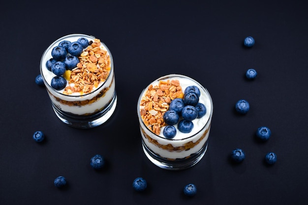 Homemade baked granola with yogurt and blueberries in a glass on a black background Space for text or design