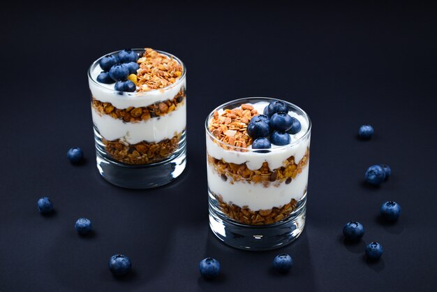 Homemade baked granola with yogurt and blueberries in a glass on a black background. Space for text or design.