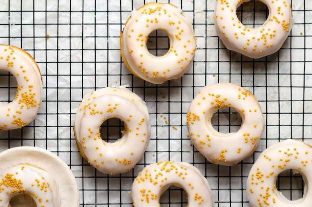 Homemade baked iced donuts with golden pearls on a black rack.