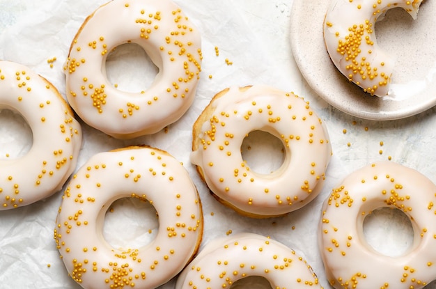 Homemade baked iced donuts with golden pearls on a white plate and on baking paper.