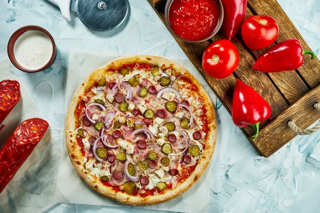 Homemade baked meat pizza with onions, cheese, ham, pickled cucumbers with red sauce. Composition with crispy pizza, tomatoes