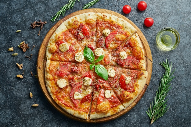 Homemade baked pizza margherita with tomatoes and mozzarella, red sauce on a black surface in a composition with ingredients