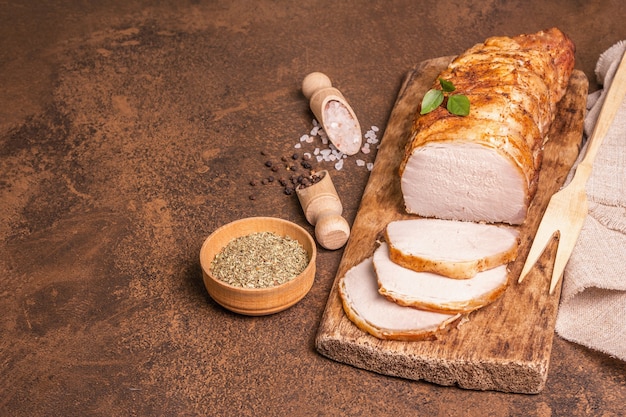 Homemade baked pork tenderloin on stone concrete background. Whole roasted piece, cut slices with spices, flat lay, copy space