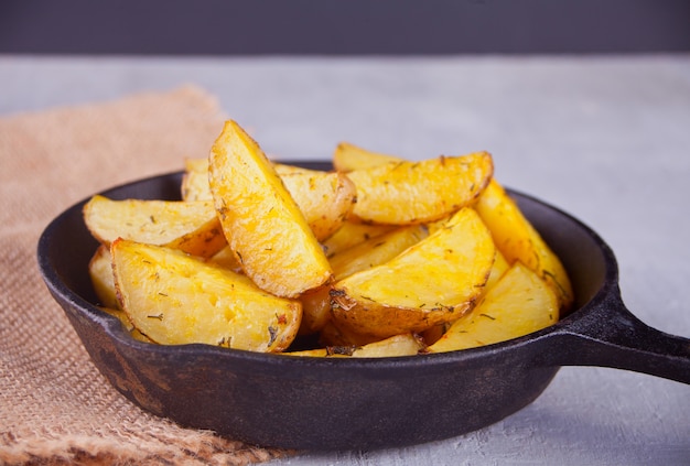 Homemade baked potato wedges with herbs on black iron pan on the gray background.