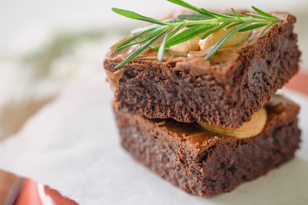 Homemade bakery dark chocolate fudge brownies cake topping with\
cashew nut and rosemary stacked on white paper with copy space.\
delicious bitter sweet and chewy. brownie is one type of chocolate\
cake.