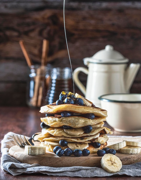 Photo homemade banana blueberry and honey pancakes on a wooden board background with cup and coffee pot