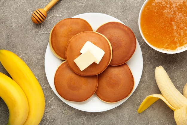 Homemade banana pancakes with butter in plate on grey background