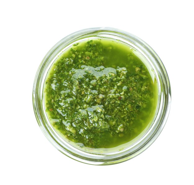 Homemade basil pesto sauce in glass jar on white background top view