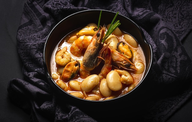 Homemade bean stew with prawns and mussels on dark background. Typical Spanish food