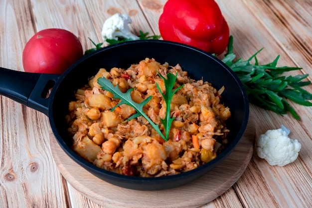 Homemade beef stew with red wine, vegetables, potato, onion, carrot, cauliflower, pepper with tomato sauce, garlic and herbs in a frying dish on wooden table. Rustic food on wooden background