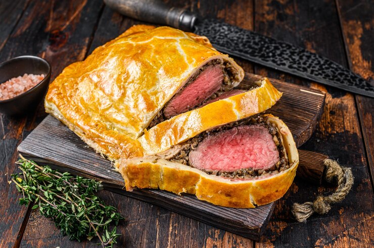 Photo homemade beef wellington puff pie with tenderloin meat on a cutting board. dark wooden background. top view.