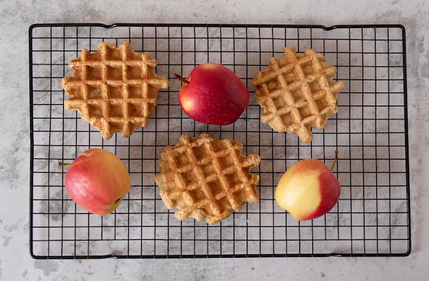 Homemade Belgian apple waffles on a grill with red apples on a gray texture background