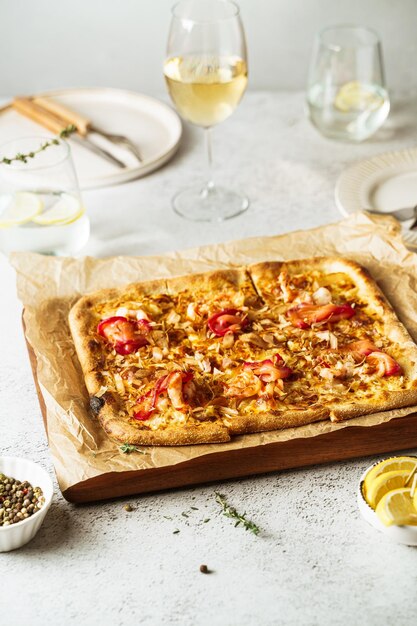 Foto pizza di frutti di mare in stile belga fatta in casa, flammekeuche servita con vino bianco.