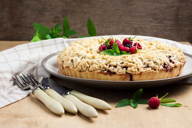 Homemade berry shortcrust pie with crumble on a plate on wooden table. Copy space