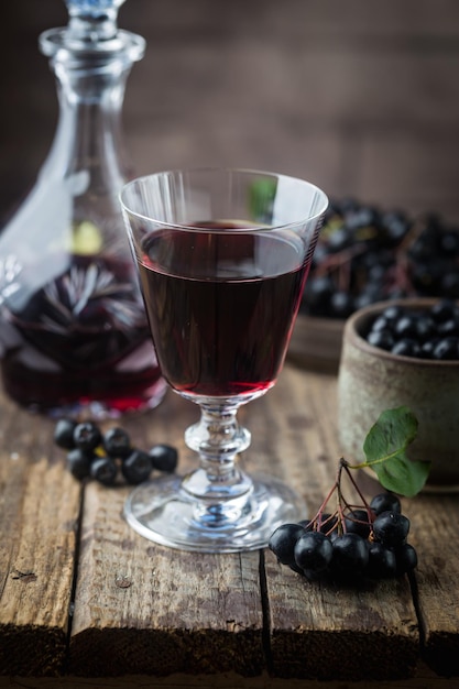 Homemade black chokeberry wine or liqueur with ripe berries on wooden background