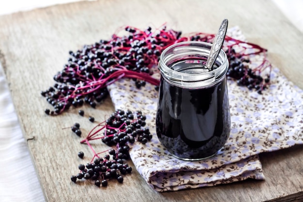 Homemade black elderberry syrup in glass jar and bunches of black elderberry in background